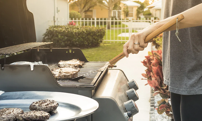 Mies seisoo puutarhassaan grillaamassa lihaa kaasugrillillä 