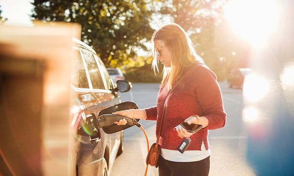 Nainen lataa sähköautoa parkkipaikalla