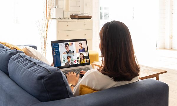 Woman sitting on couch while attending a meeting on her laptop